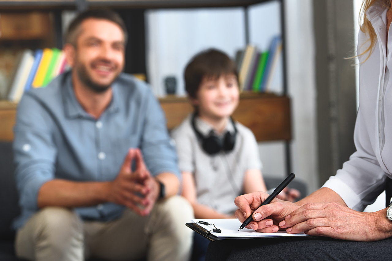 cropped image of female counselor writing in clipboard while father and son sitting on therapy