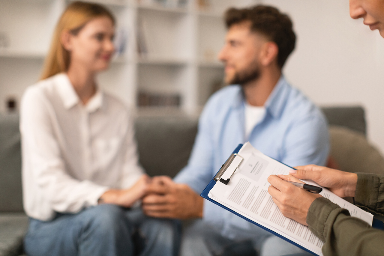 Psychotherapist takes notes on tablet during successful counseling session indoor Psychotherapist lady takes notes on tablet during successful counseling session, while young married couple holding hands after reconciliation in modern office. Selective focus